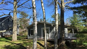 A small, single-story cabin with a porch, surrounded by trees and a clear blue sky.