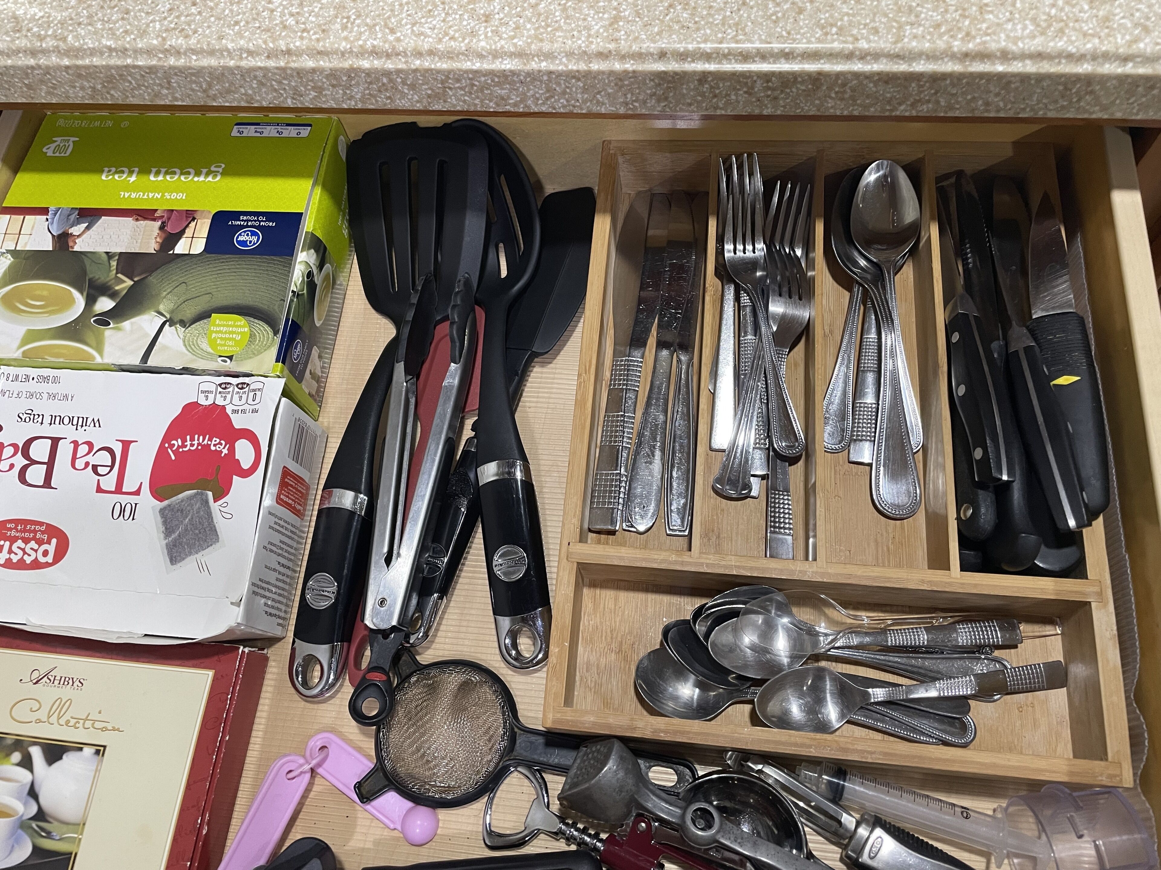 Eine Schublade mit verschiedenen Küchenutensilien, darunter Messer, Löffel und eine Reibe.