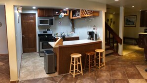 A kitchen with a central island, bar stools, a microwave, oven, and a coffee maker.