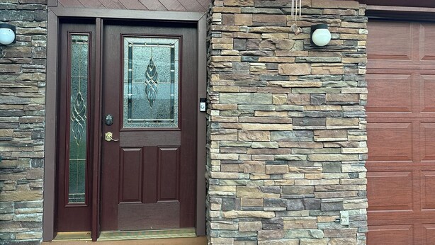 A house with a brown door, a stone wall, and a garage door.