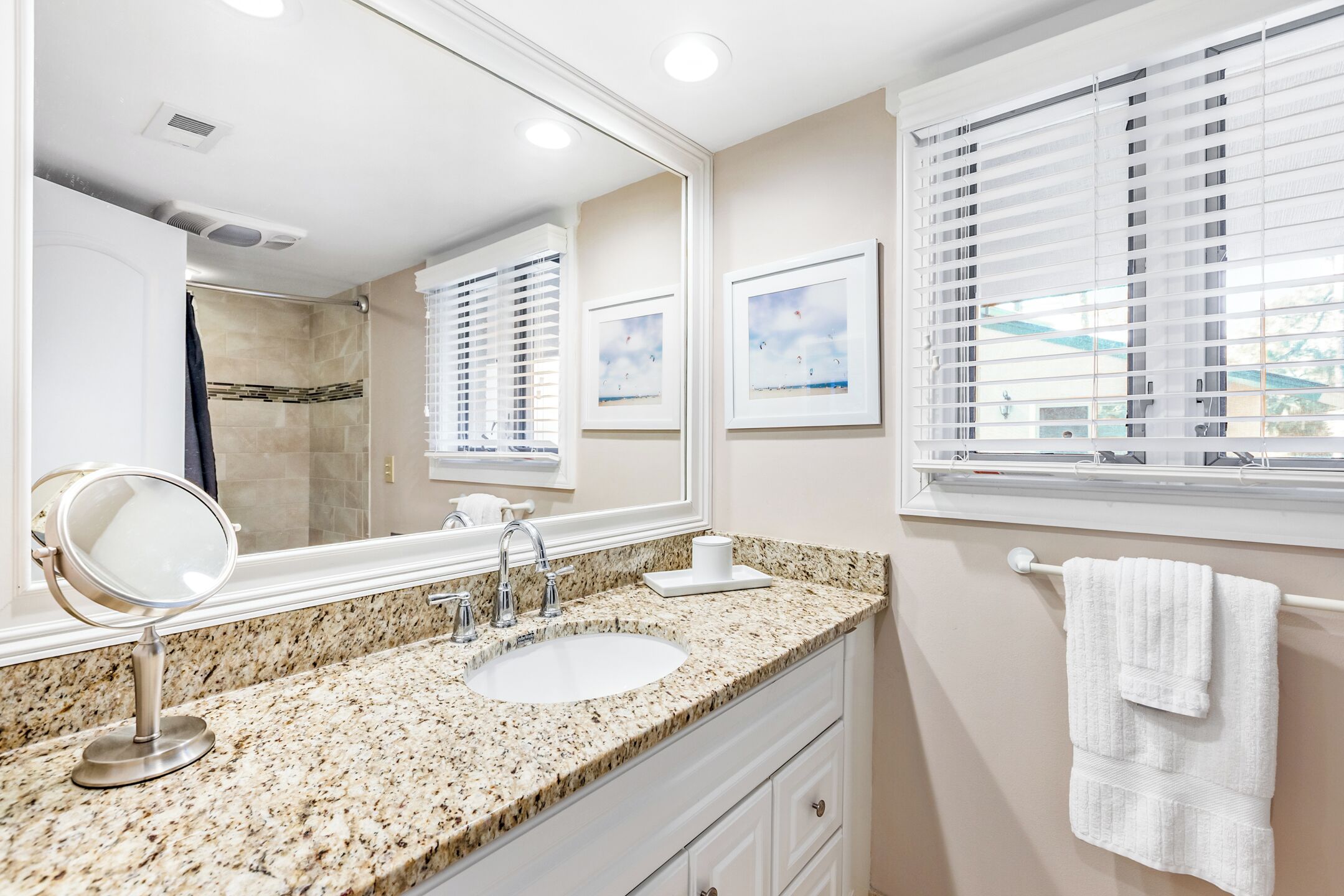 A bathroom with a granite countertop, a sink, a mirror, and a window with blinds.