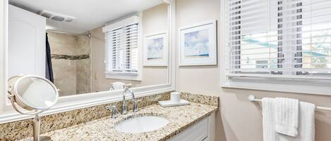 A bathroom with a granite countertop, a sink, a mirror, and a window with blinds.