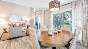 A dining area with a round wooden table, wicker chairs, and a hanging light fixture.