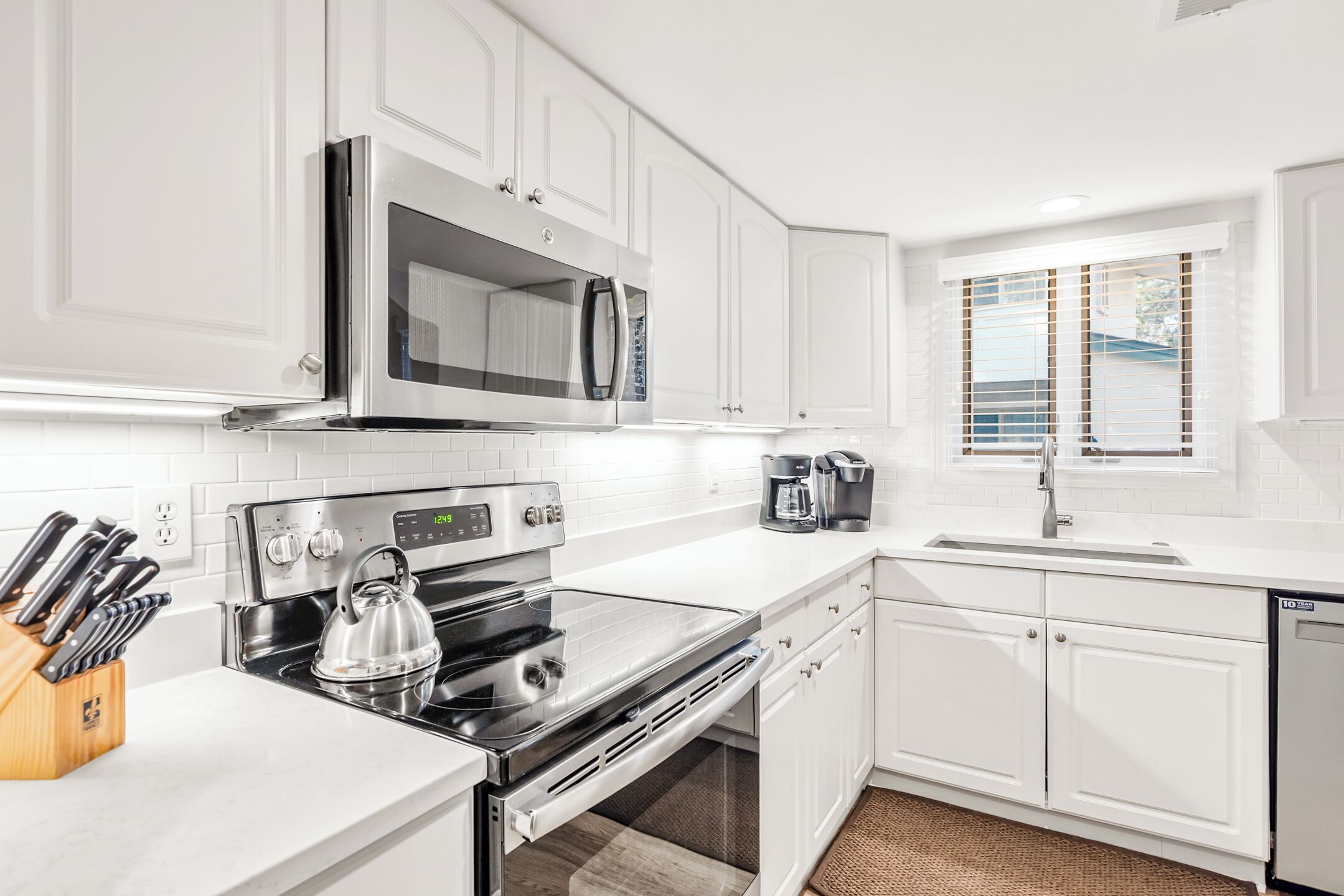 A modern kitchen with white cabinetry, a stainless steel stove, a microwave, and a coffee maker.