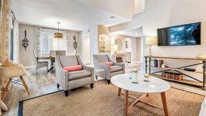 A spacious living room with two grey armchairs, a white coffee table, and a TV mounted on the wall.