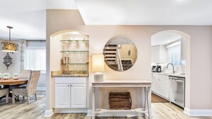 A modern kitchen with white cabinets, a round mirror, and a dining area with wicker chairs.