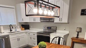 A modern kitchen with white cabinets, a wooden dining table, and a built-in oven. - Fun Under The Sun, Condo 3: You Need a St. George Get-away! (St George)