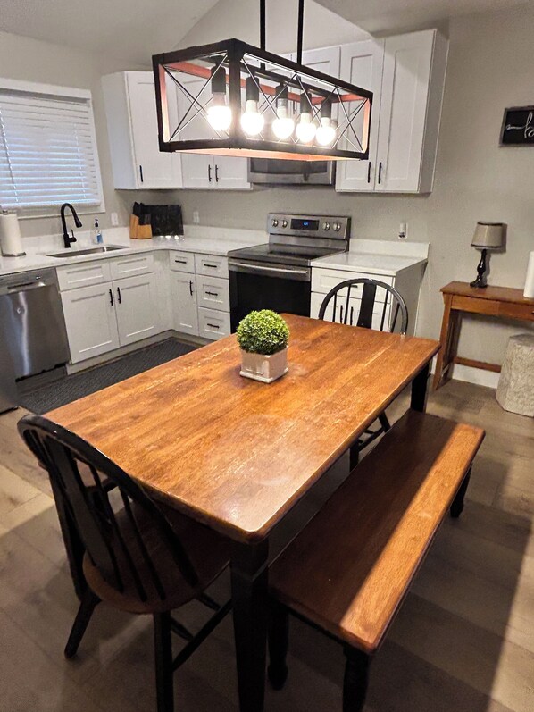 A modern kitchen with white cabinets, a wooden dining table, and a built-in oven.