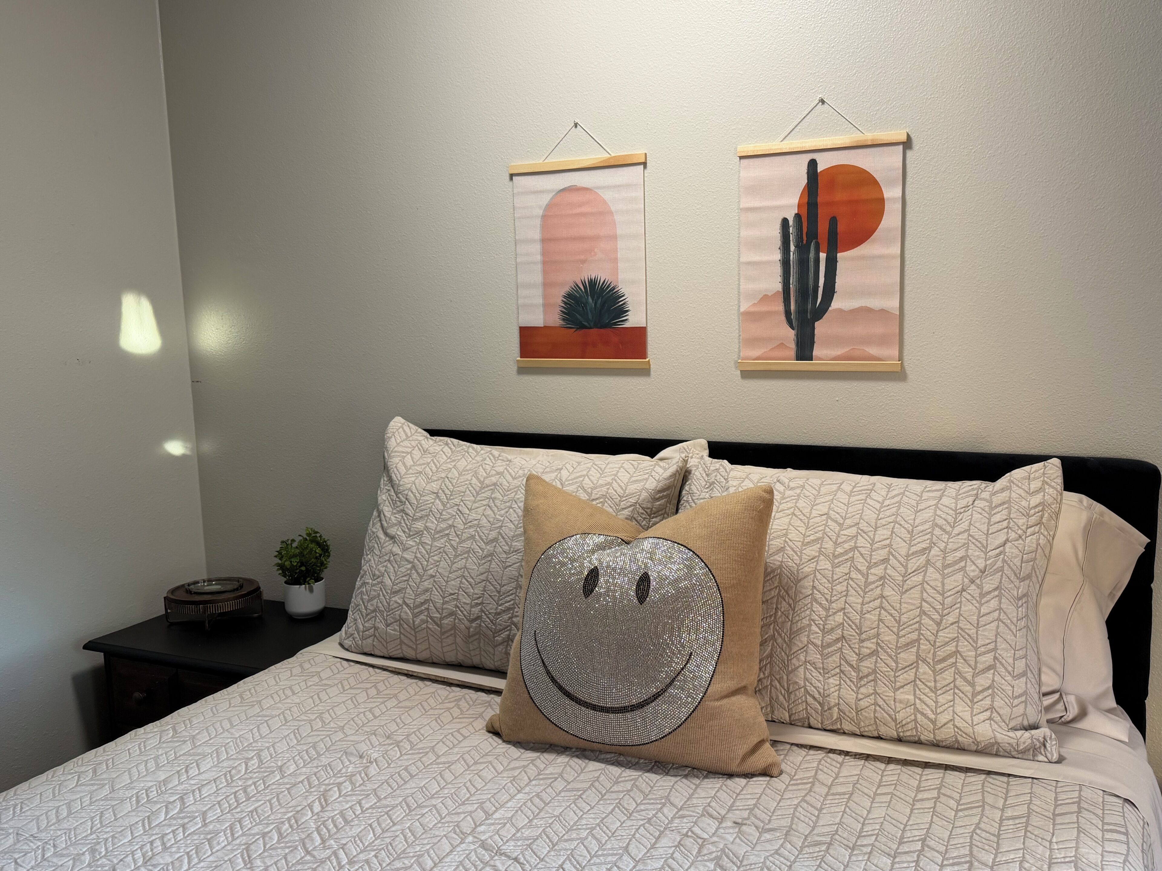 Ein Schlafzimmer mit einem Bett, zwei Kissen, einem Nachttisch mit Pflanze und zwei Wandbildern.