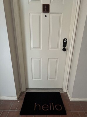 A white door with a numbered lock plate, a doorbell, and a black doormat with the word "hello".
