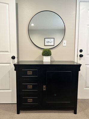 A black cabinet with drawers and a large mirror above it, set against a plain wall with a small potted plant on top.