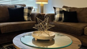 A round glass coffee table with a wooden base and metal legs, featuring a geometric metal sculpture. - Fun Under The Sun, Condo 3: You Need a St. George Get-away! (St George)