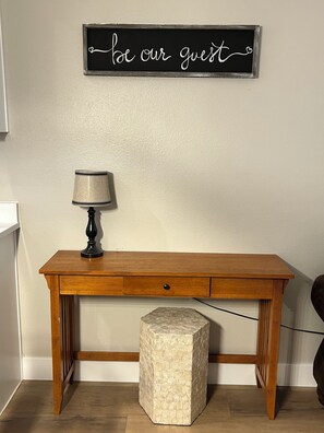 A wooden desk with a lamp and a decorative sign above it.