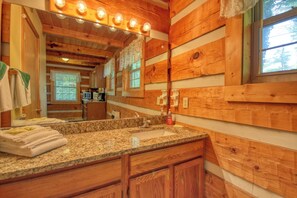 A wooden cabin bathroom with a granite countertop, sink, and wooden cabinets.