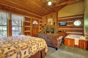 Una habitación tipo cabaña de madera con cama, chimenea, sofá, bañera y un ventanal grande.