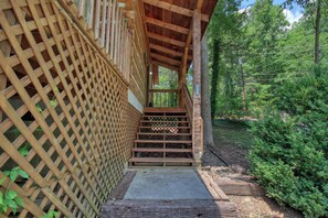 A wooden staircase leading to a covered area with a lattice wall and a view of a forested area.