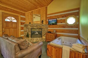 A wooden interior with a stone fireplace, a large wooden door, a sofa, a wooden cabinet, and a hot tub. - Gatlinburg | Hot Tub | Pet Friendly | Fireplace (GATLINBURG)