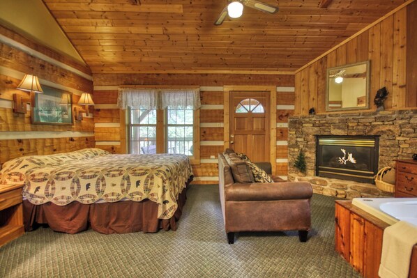 Un dormitorio de estilo cabaña de madera con cama, sofá, chimenea y pared de piedra.