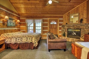 A log cabin-style bedroom with a bed, a sofa, a fireplace, and a stone wall.