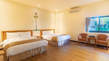 A hotel room with two beds, a wooden floor, a window with a view, wicker chairs, and an air conditioning unit.