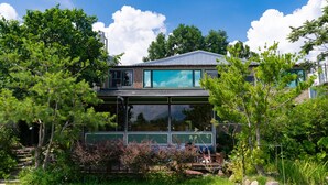A modern house with large windows, surrounded by lush greenery and trees. - Lane 523 (Puli)