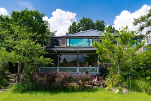 A modern house with large windows, surrounded by lush greenery and trees.