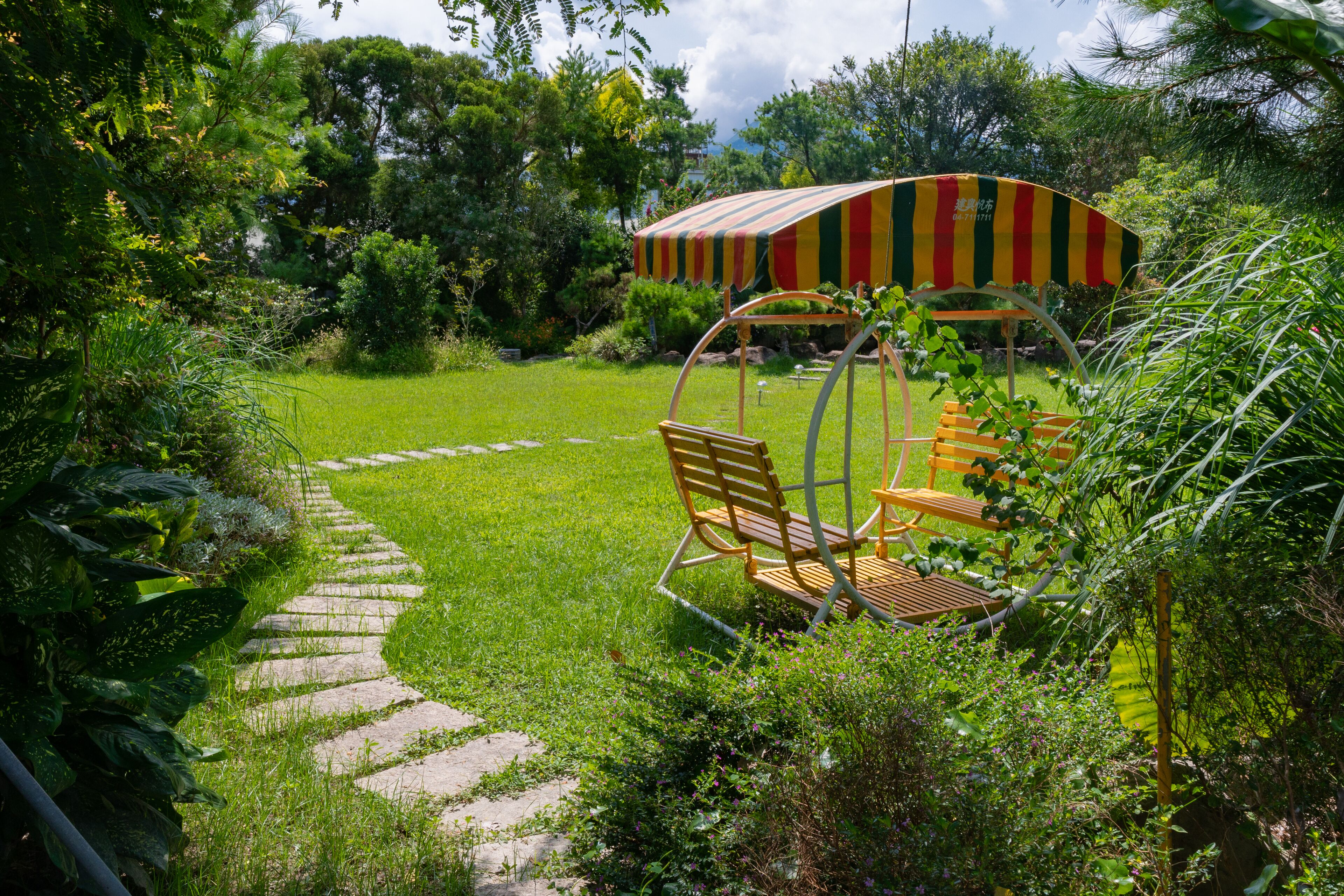 A garden with a stone pathway, a swing chair, and a striped canopy.