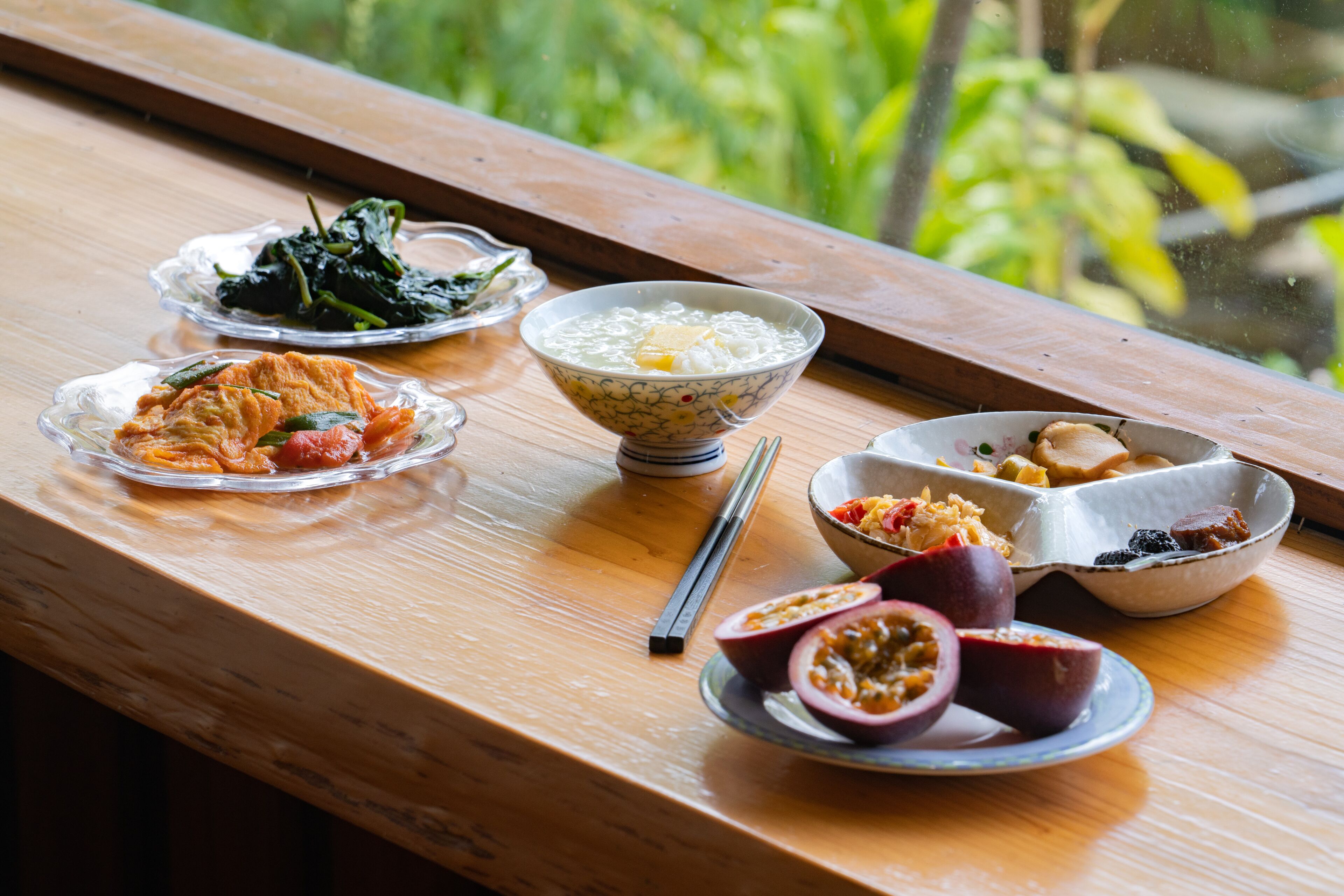 A wooden table with various dishes, including a bowl of rice, a plate of vegetables, and a bowl of fruit.