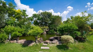 A serene garden with a pond, lush greenery, and a clear blue sky. - Lane 523 (Puli)