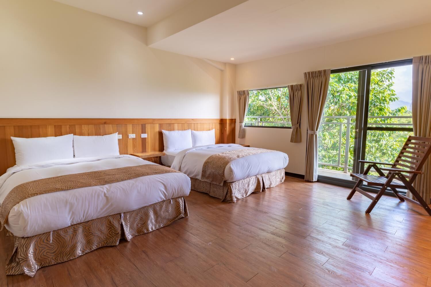 Ein Hotelzimmer mit zwei Betten, einem Holzkopfende, Holzboden und einem Balkon mit einem Stuhl.