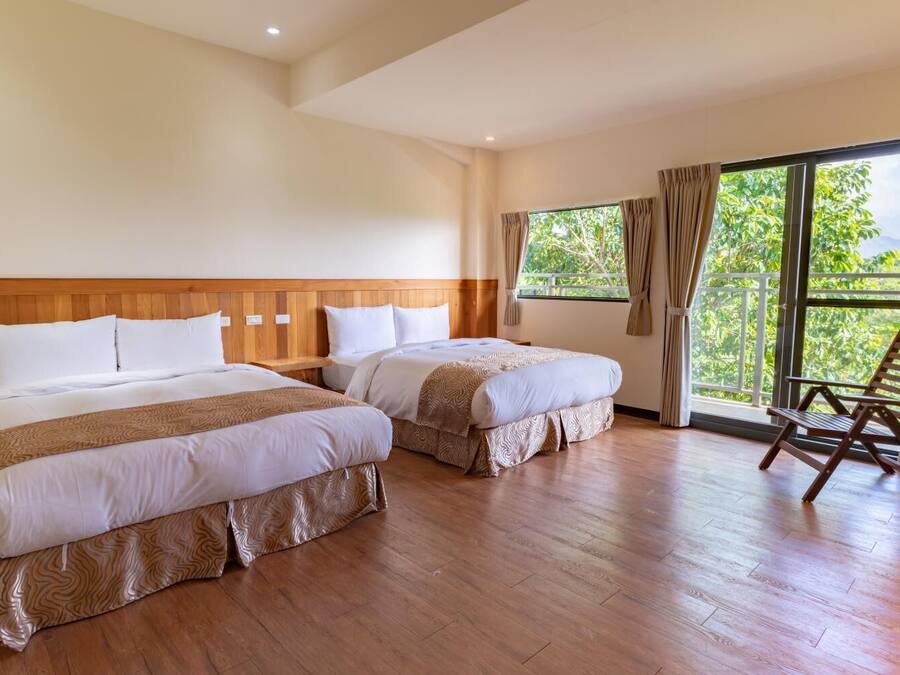 A hotel room with two beds, a wooden headboard, a wooden floor, and a balcony with a chair.