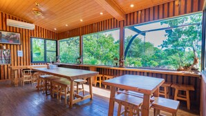 A wooden interior with large windows, wooden tables and benches, and a ceiling fan. - Lane 523 (Puli)