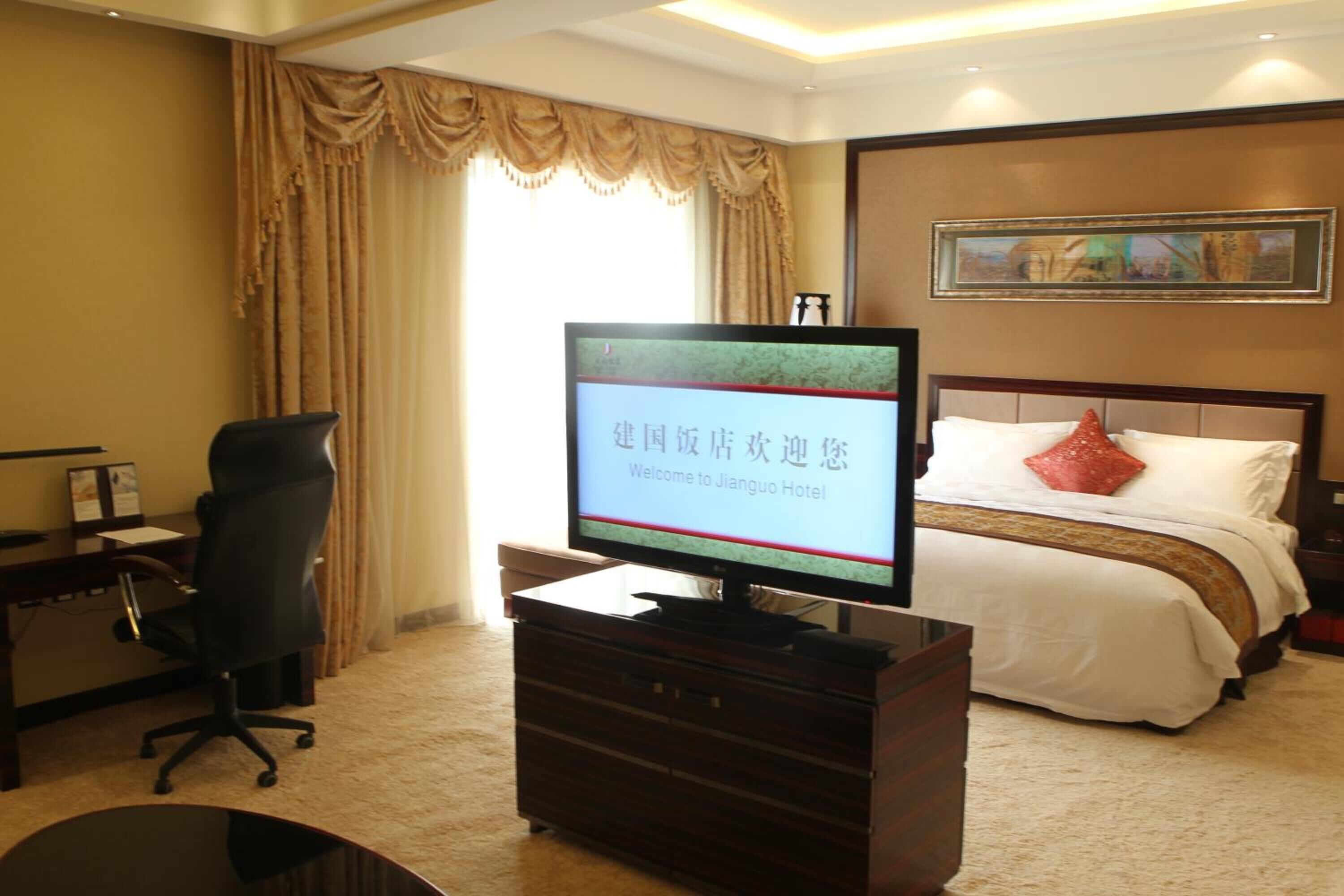 Une chambre d’hôtel équipée d’un lit, d’un bureau, d’une chaise, d’une télévision et d’une fenêtre avec des rideaux.