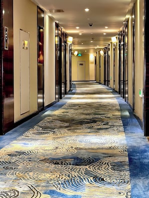 A hotel corridor with a patterned carpet, doors on both sides, and overhead lighting.