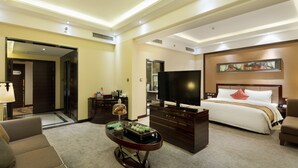 A hotel room with a large bed, a flat-screen TV, a wooden dresser, a coffee table, and a sofa.