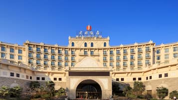 Un hotel grande de varios pisos con una entrada destacada y un cielo azul brillante.