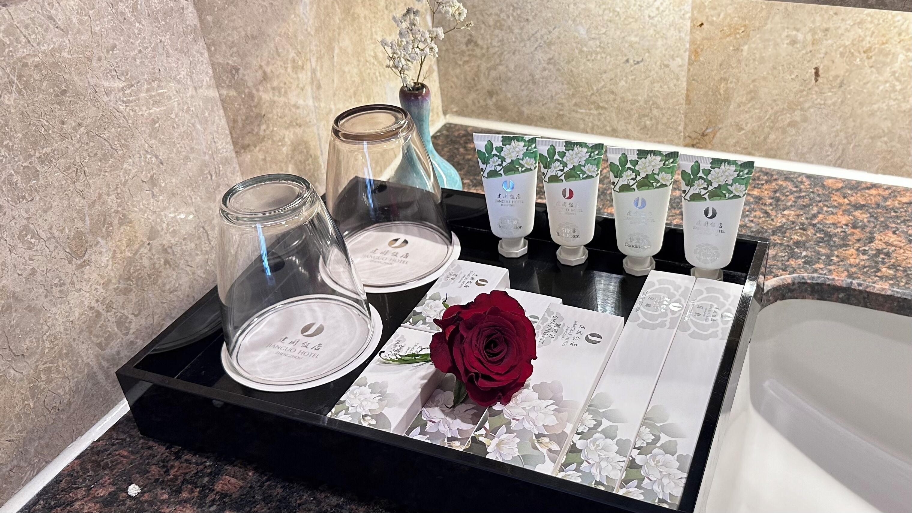 Un meuble-lavabo de salle de bain agrémenté d’un bocal en verre, d’un vase avec des fleurs et d’une rose rouge posée sur un plateau.