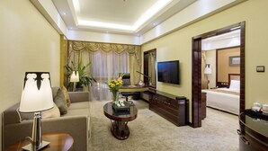 A hotel room with a sofa, a coffee table with a vase of flowers, a TV, a desk with a chair, and a bed.