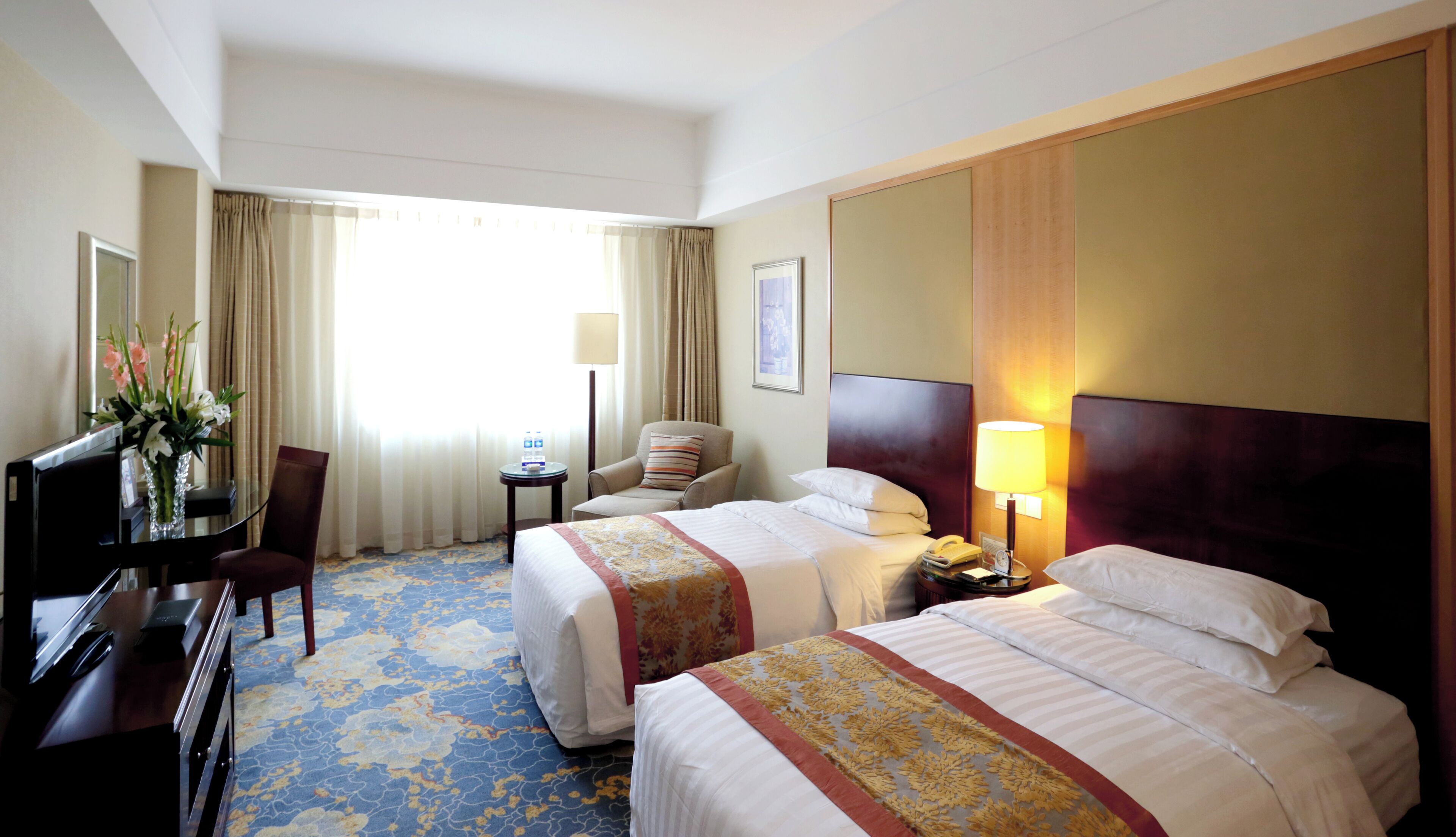 Habitación de hotel con dos camas, un escritorio con computadora, una silla, una lámpara y una ventana con cortinas.