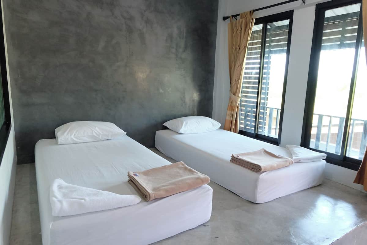 Habitación de hotel con dos camas, una pared de concreto y un balcón con vistas.