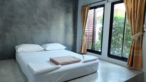 A single bed with white linens, a beige blanket, and two pillows. There is a window with curtains, and a view of greenery outside. - Numjaan Resort (Krabi)