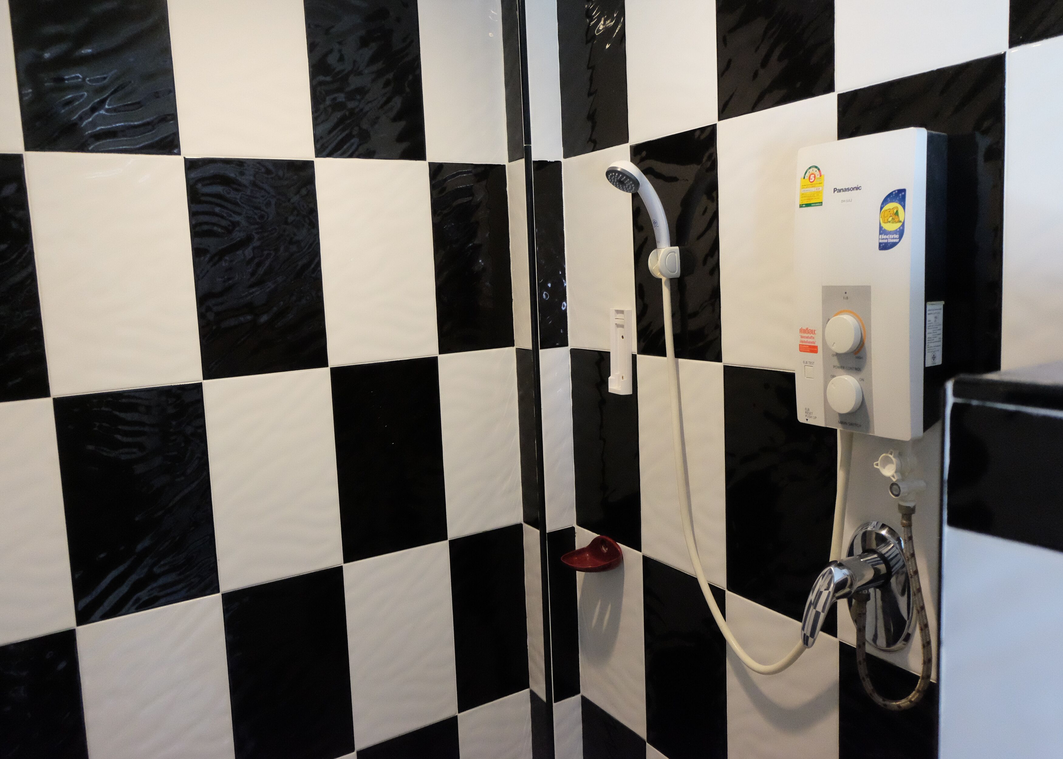 A bathroom with black and white checkered tiles, a white showerhead, and a control panel with a Panasonic logo.