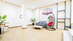 A modern living room with a grey sofa, a round coffee table, a hanging chair, and a wall-mounted shelf. - Le Paris Syariah Residence (Tangerang)