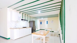 A modern kitchen with white cabinets, a wooden countertop, and a stainless steel refrigerator. There is a dining area with a wooden table and white chairs. - Le Paris Syariah Residence (Tangerang)
