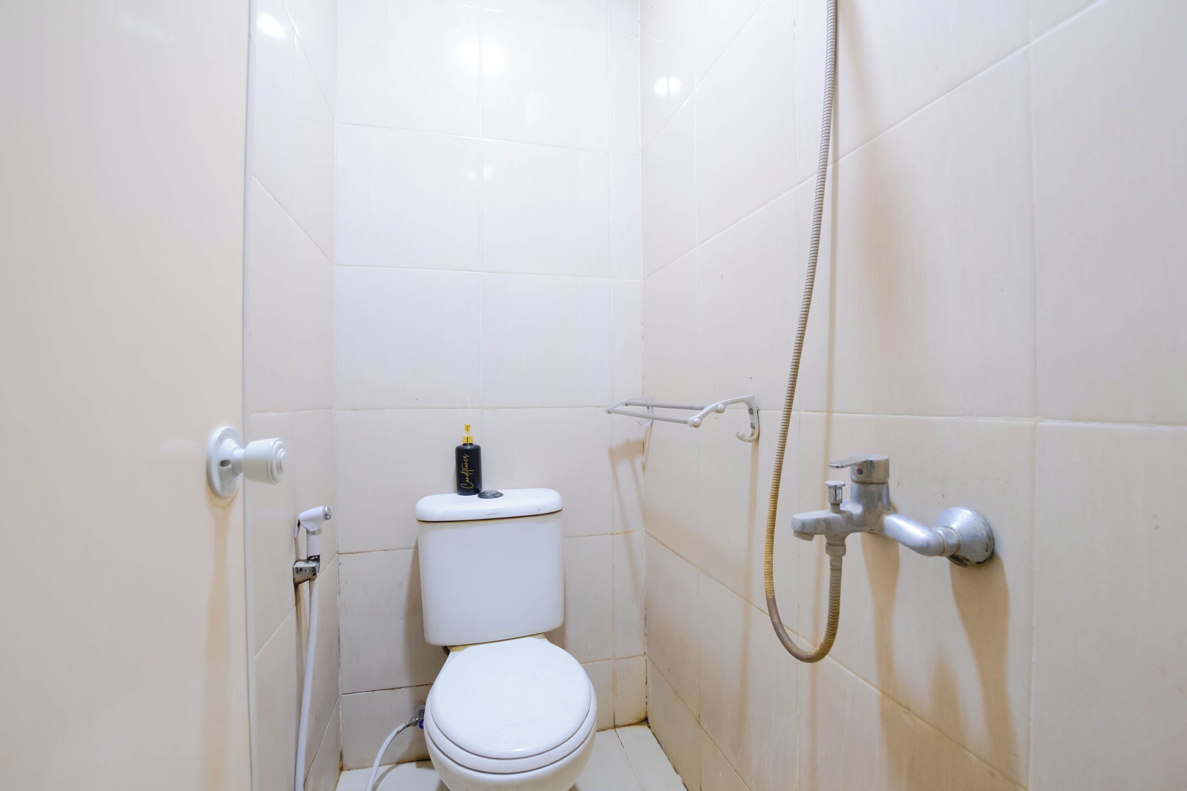 Een kleine badkamer met witte tegels, een toilet, een douche en een handdroger.