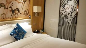 Una habitación de hotel con una cama grande, una mesita de noche, una lámpara, una pared con un mural de ciervo y una puerta corredera con estampado a rayas.