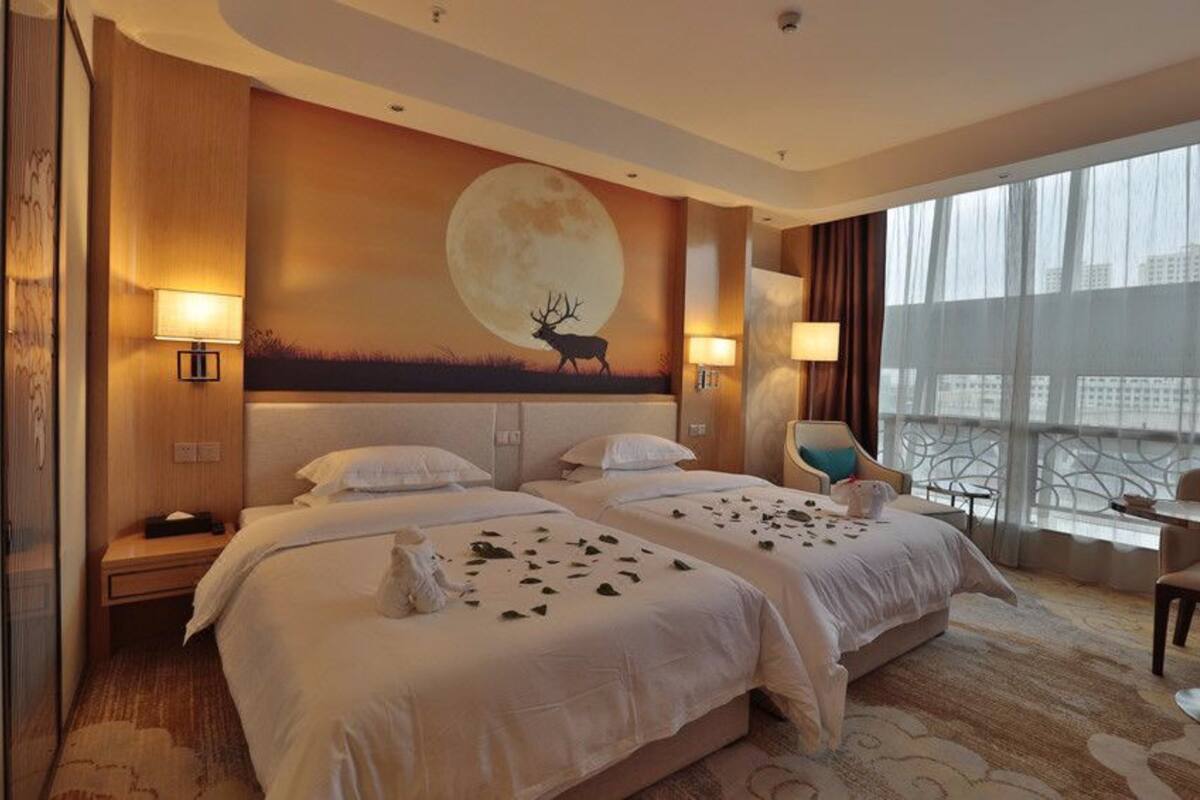 Une chambre d’hôtel avec deux lits, une grande fresque murale représentant un cerf et la lune, et une vue sur le paysage urbain à travers de grandes fenêtres.