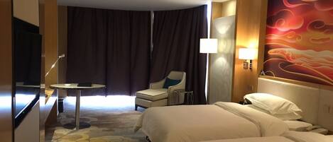 A hotel room with two beds, a desk, a chair, a TV, and a wall with a red abstract design.