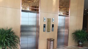 A modern elevator area with metallic doors, a small decorative column, and potted plants. - Qinghai Baiyun Xiangling Hotel (Xining)