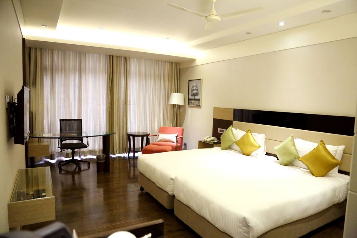A hotel room with a large bed, a desk, a chair, a television, and a ceiling fan.